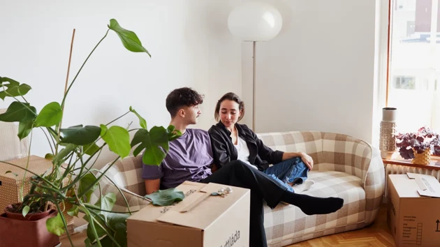 En man och en kvinna sitter i en soffa i ett vardagsrum, omgivna av flyttkartonger.